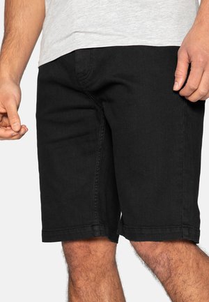 Shorts en jean noir, coupe ajustée, coupe droite, détails de couture visibles et ourlets retroussés. Le matériau semble durable avec une texture lisse.