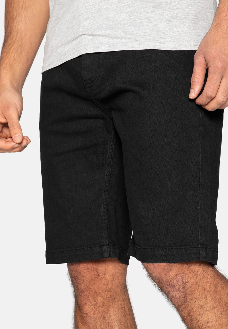 Shorts en jean noir, coupe ajustée, coupe droite, détails de couture visibles et ourlets retroussés. Le matériau semble durable avec une texture lisse.