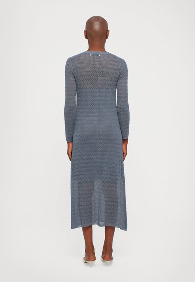 Rochie tricotată lungă, ajustată, de culoare albastră, cu un design texturat, dintr-o țesătură deschisă. Dispune de mâneci lungi și o lungime până la jumătatea gambelor, lăsând la vedere piciorul la capăt.