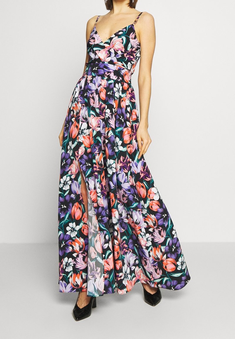 Robe maxi fleurie présentant des motifs multicolores de tulipes et d'orchidées sur un fond sombre, avec des bretelles fines et une fente latérale.