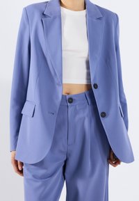 Lichtpaarse blazer van gladde stof, met een geknipte kraag, twee knopen en een getailleerde pasvorm met klepzakken. Gecombineerd met bijpassende broek.