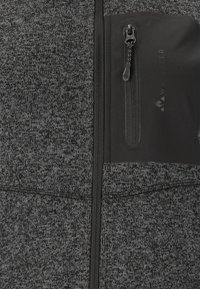 Veste zippée gris et noir en tissu texturé, dotée d'une poche poitrine zippée avec bord noir et détail de logo.
