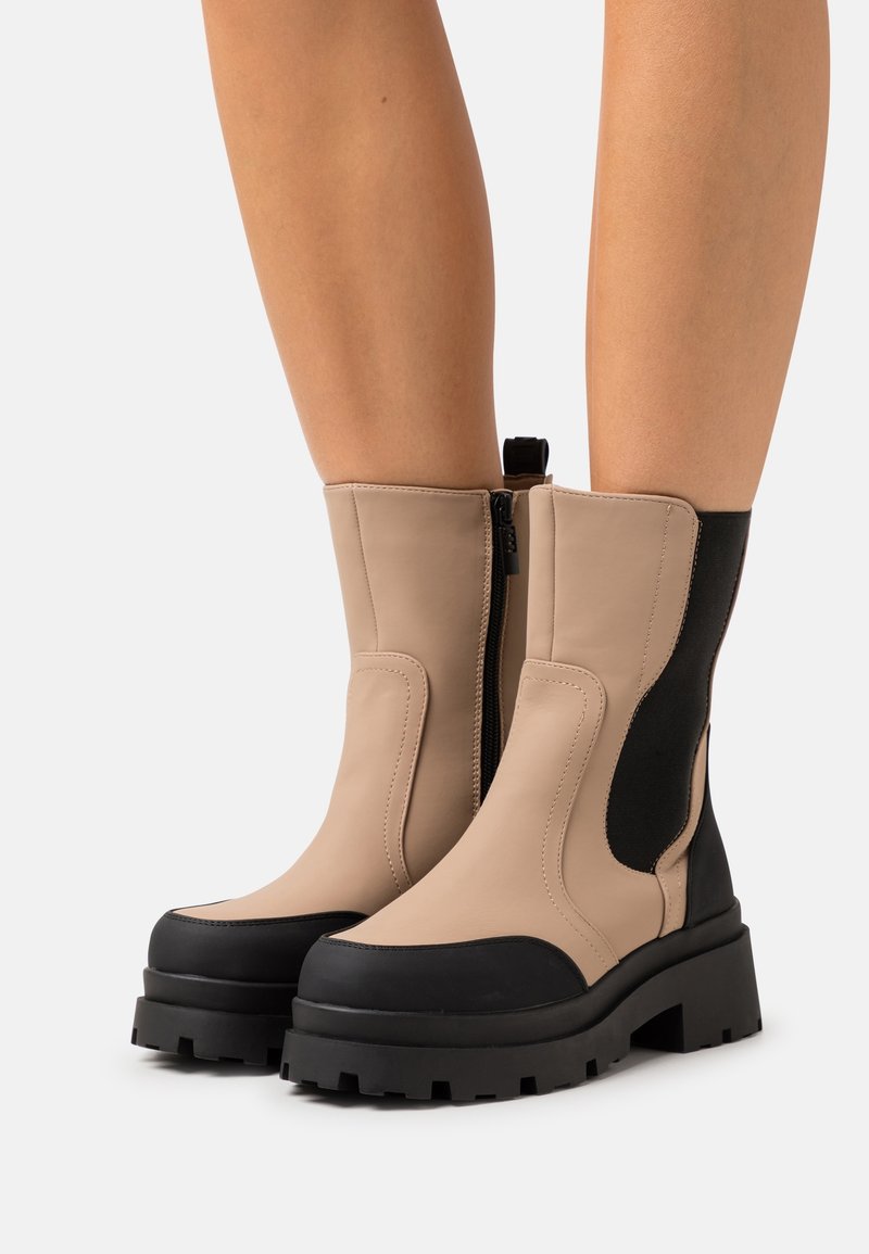Bottes cheville en cuir marron clair et noir avec talon bloc, équipées d'une fermeture éclair latérale et d'un panneau élastique pour plus de flexibilité, ainsi qu'une semelle robuste.