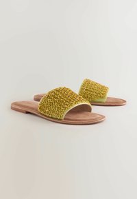 Chanclas amarillas trenzadas con diseño de punta abierta, plantillas de suave color marrón y superficie texturizada. Suela ligera y plana.
