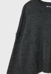 Pull en maille gris foncé avec col rond, poignets et ourlet côtelés, montrant un tissu texturé et un léger design à épaules tombantes.