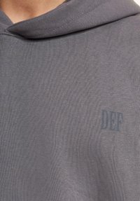 Gray hoodie featuring a textured fabric, adjustable drawstring hood, and a small printed "DEF" logo on the front.