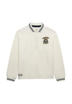 Hvid poloshirt med lange ærmer og stribet krave og manchetter, med et broderet våbenskjold i marineblåt og guld på venstre bryst.