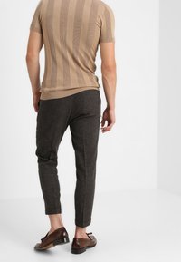 Beige trui met korte mouwen van gebreide stof met verticale ribbelstructuur, gecombineerd met donkere grijze tapering broek en bruine instappers.