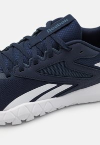 Basket de sport bleu marine en mesh et matériau synthétique, avec des accents blancs, une surface texturée et une semelle extérieure blanche robuste.