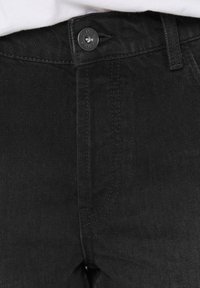 Schwarze Jeans aus Denim mit mittlerem Bund, Knopfverschluss und tonalem Nähen, die eine glatte Textur und ein modernes Design präsentieren.