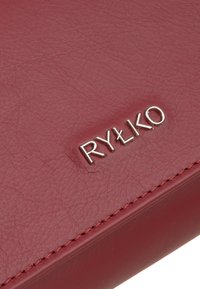 Portafoglio in pelle bordeaux Rylko con texture liscia, logo impresso e dettagli di cucitura a contrasto lungo il bordo. Forma compatta e rettangolare.