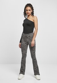 Bodysuit nero a spalla unica abbinato a pantaloni grigi chiari a palazzo con motivo zebrado. Sneakers bianche completano l'outfit.