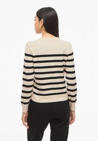 Beige sweater with black horizontal stripes, crew neck, and long sleeves. Fabric appears soft, with ribbed cuffs and hem detail.