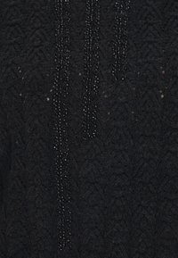 Schwarzer Strickpullover mit einem strukturierten Muster und Perlenverzierungen, die vertikal auf der Vorderseite hängen. Weicher Stoff mit einem warmen Aussehen.