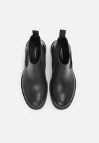 Črne usnjene gležnjarje z elastiko ob straneh in zanka za peto. Gladka tekstura, okrogla konica in ozka gumijasta podplat. Logotip blagovne znamke viden znotraj.