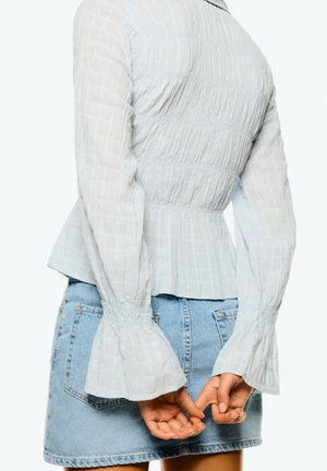 Jasnoniebieska, teksturowana bluzka z długim rękawem, z marszczonymi detalami i rozszerzającymi się mankietami, w połączeniu z dżinsową spódniczką mini z tylnymi kieszeniami.