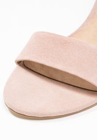 Sandale à bout ouvert en daim rose clair avec une large bride sur l’avant et une semelle plate.