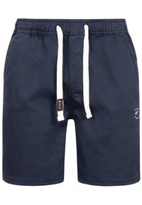 Shorts de bain bleu marine en tissu léger. Ils comportent un cordon blanc, des poches latérales et un petit logo sur le devant à gauche.