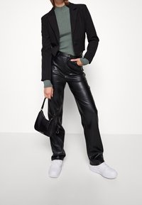 Czarna krótka marynarka na zielonym swetrze, zestawiona z wysokim stanem czarnych spodni ze sztucznej skóry oraz białymi trampkami. W zestawie mała czarna torebka.