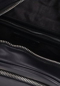 Interno di una borsa in pelle nera con zip argentata, caratterizzato da una superficie liscia e una sottile fodera in tessuto all'interno. Sono visibili due scomparti.