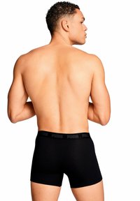 Boxer briefs de algodón negro con una cintura de logo, diseño ajustado y material elástico, mostrados desde la parte trasera sobre un fondo neutral.