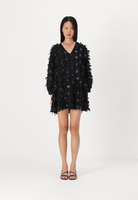 Vestido preto com aplicações florais e lantejoulas, apresentando um decote em V profundo e mangas longas, tecido texturizado e um corte solto.