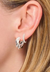 Orecchino ad anello in argento a spirale abbinato a un piccolo pezzo accentuato curvo e scintillante, che mette in risalto texture lisce e finiture lucide.