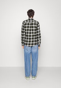 Černobílé kostkované flanelové košile s dlouhými rukávy a klasickým límečkem, spárované s volnými modrými džíny a zelenými botami.