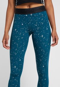 Leggings en color azul verdoso con un estampado estrellado, que cuentan con una cinturilla elástica negra. El material es suave y elástico, adecuado para ropa deportiva.