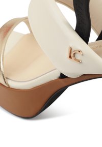 Sandalía cuña con parte superior de cuero beige y detalles metálicos dorados, tiras negras y suela de plataforma marrón; incluye un logo dorado "LC".