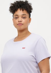 Camiseta de algodón color púrpura claro con cuello redondo y mangas cortas. Presenta un logo rojo de Levi's en el lado izquierdo del pecho. Textura suave.