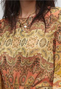 Vestido con un patrón de paisley multicolor en tonos de naranja, amarillo y crema; tejido ligero con una textura suave y un diseño fluido.