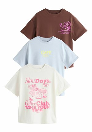 Drei übergroße T-Shirts: braun mit pinkem Grafikdruck, hellblau mit gelbem Text und cremefarben mit pinken Illustrationen und Text; alle aus Baumwolle.