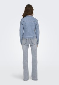 Chaqueta de mezclilla azul clara de corte slim, con cuello clásico y dos bolsillos en la parte trasera. Combinada con jeans acampanados gris claro que presentan costuras visibles.