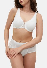 Hvid bh med bløde skåle og blonder, parret med matchende hvide trusser med et subtile blomstermønster. Glat stof, sømløs design.