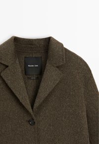 Cappotto in misto lana di un verde scuro, texture a rilievo, con colletto a punte, chiusura con un bottone e etichetta interna. Tessuto morbido e caldo.