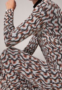 Robes à manches longues présentant un motif en vagues dans des teintes de blanc, marron et noir. Fabriquée en tissu texturé avec une coupe ajustée.