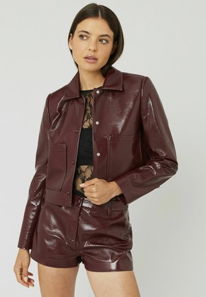 Veste en cuir synthétique bordeaux cropped avec col pointu, deux poches avant et boutons pression, assortie avec un short taille haute.