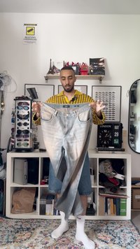 Fakó kék farmer, elülső részén világosabb árnyalattal, két zsebbel és karcsú fazonban, semleges háttér előtt tartva.