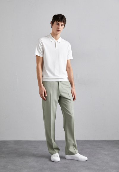 Hvit polo skjorte med korte ermer kombinert med lysegrønne skreddersydde bukser. Modellen har på seg hvite sneakers. Enkelt design, jevne teksturer.