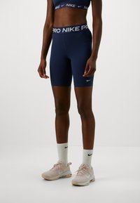 Person som bär marinblå Nike Pro-shorts, vita Nike-strumpor, beige Nike-sneakers och en matchande marinblå Nike sport-bh.