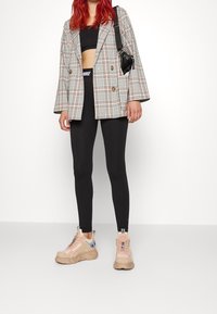 Rutig dubbelknäppt blazer i grå och ljusa färger, svart crop top, svarta leggings och chunky sneakers med rosa detaljer.
