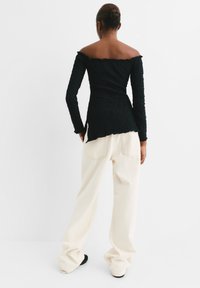 Zwarte off-shoulder top van textuurstof, met lange mouwen en een golvende zoom, gecombineerd met crème-kleurige wijde broek.