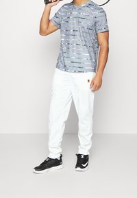 Camiseta atlética de manga corta a rayas grises y verdes combinada con pantalones de chándal blancos y zapatillas deportivas negras con acentos blancos.