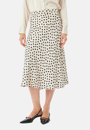 Jupe couleur crème avec des pois noirs, design évasé, texture lisse, longueur au genou, portée avec des ballerines noires à bout pointu.