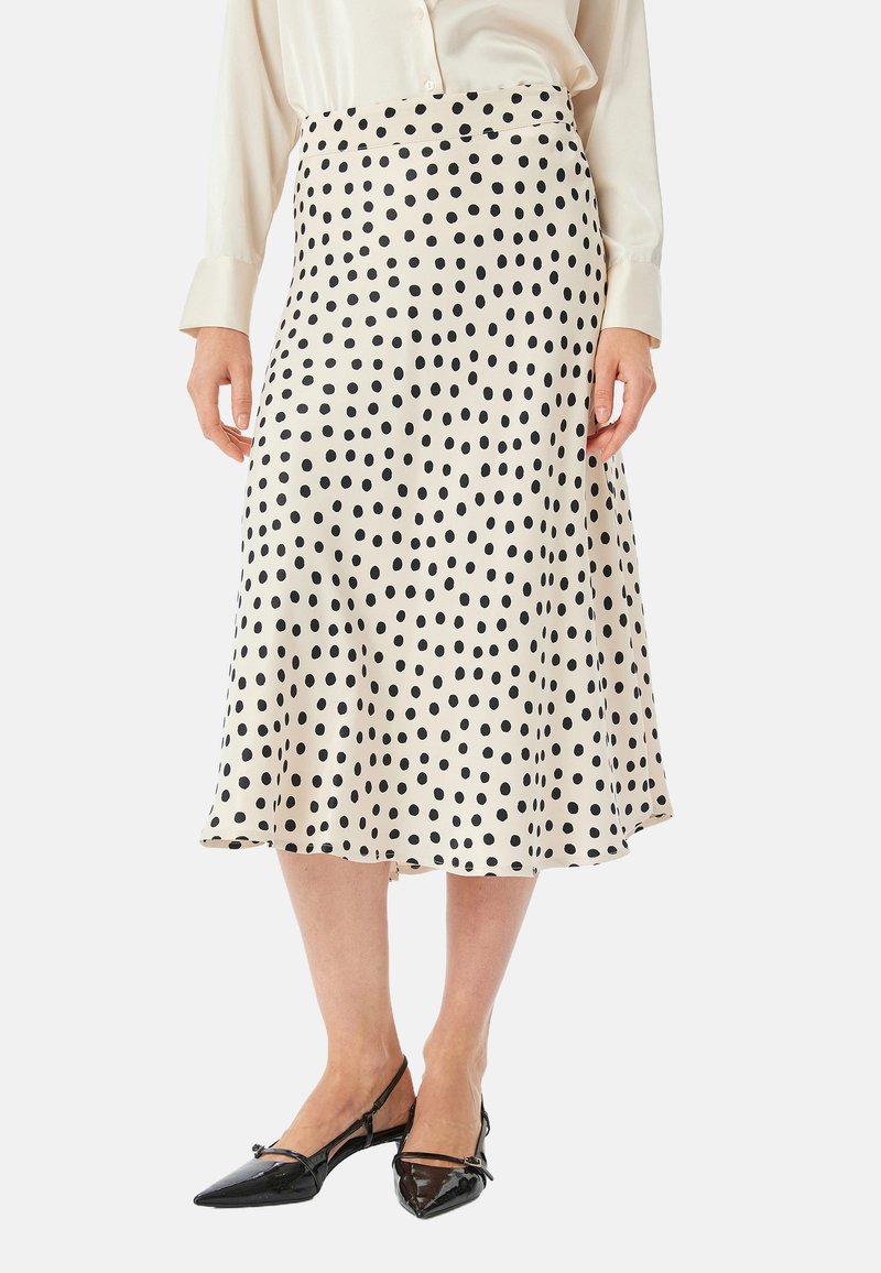 Crème-kleurige rok met zwarte stippen, uitlopende ontwerp, gladde textuur, knielang, gedragen met zwarte puntige flats.