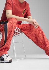 Czerwona koszulka graficzna z żółtym napisem w połączeniu z wzorzystymi czerwonymi spodniami dresowymi z granatowymi i żółtymi akcentami. Białe i czarne sneakersy.