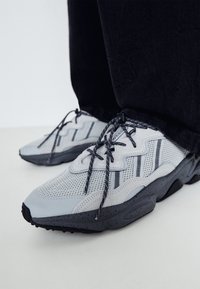 Gray mesh athletic shoes with dark gray soles, textured material, black laces, and side stripes. The toe has a rounded shape and reinforced design.