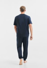 Completo da casa in blu navy composto da una t-shirt a maniche corte con collo tondo e pantaloni affusolati coordinati con polsini elasticizzati, realizzati in tessuto morbido.