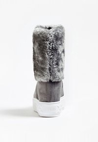 Botín de ante gris con puño de pelaje sintético, suela de goma blanca y detalles texturizados en el tacón. En la parte inferior se encuentra el nombre de la marca "GUESS."